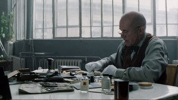 Movie still from “Munich” (2005), directed by Steven Spielberg – An older man sitting at a table with a lot of papers; Medium shot, Low angle