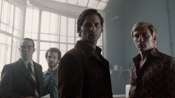 Movie still from “Munich” (2005), directed by Steven Spielberg – A group of men standing next to each other in front of a window; Medium shot, Low angle