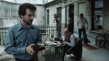 Movie still from “Munich” (2005), directed by Steven Spielberg – A man standing next to a table holding a guitar; Medium shot, Low angle