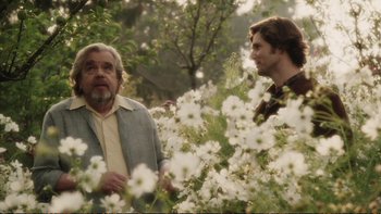Movie still from “Munich” (2005), directed by Steven Spielberg – Two men standing next to each other in a field of white flowers; Medium shot, Over the shoulder angle