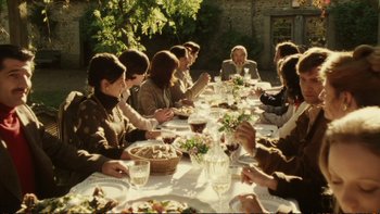 Movie still from “Munich” (2005), directed by Steven Spielberg – A group of people sitting at a long table eating food; Wide shot, High angle