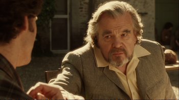 Movie still from “Munich” (2005), directed by Steven Spielberg – An older man in a suit sitting at a table; Close Up shot, Over the shoulder angle