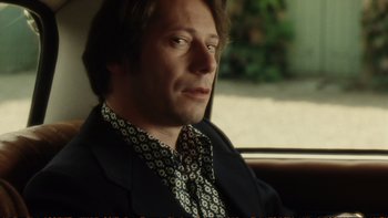 Movie still from “Munich” (2005), directed by Steven Spielberg – A person sitting in a car wearing a suit; Close Up shot, Low angle