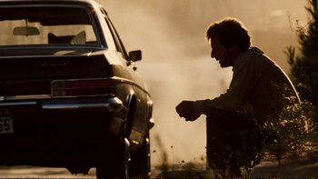 Movie still from “Munich” (2005), directed by Steven Spielberg – A man standing next to a parked car on a road; Wide shot, Low angle