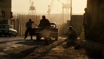 Movie still from “Munich” (2005), directed by Steven Spielberg – A man standing on the side of a road next to a car; Wide shot, Low angle