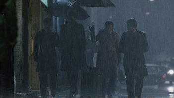 Movie still from “Munich” (2005), directed by Steven Spielberg – A group of people standing under an umbrella in the rain; Wide shot, Low angle
