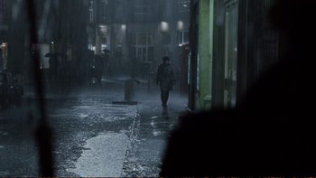 Movie still from “Munich” (2005), directed by Steven Spielberg – A man walking down a street in the rain; Wide shot, High angle