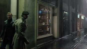 Movie still from “Munich” (2005), directed by Steven Spielberg – A man walking down the street in front of a store window; Wide shot, Over the shoulder angle