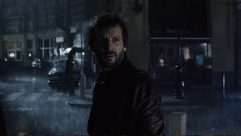 Movie still from “Munich” (2005), directed by Steven Spielberg – A man in a leather jacket standing in the rain; Close Up shot, Over the shoulder angle