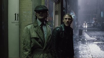 Movie still from “Munich” (2005), directed by Steven Spielberg – A couple of men standing next to each other on a street; Medium shot, Low angle