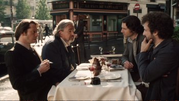 Movie still from “Munich” (2005), directed by Steven Spielberg – Two men sitting at a table in front of each other at a restaurant; Medium shot, Over the shoulder angle