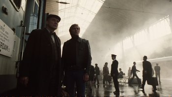 Movie still from “Munich” (2005), directed by Steven Spielberg – A couple of men standing next to each other in a building; Wide shot, Low angle