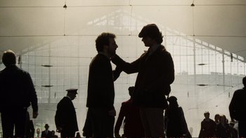 Movie still from “Munich” (2005), directed by Steven Spielberg – Two men standing next to each other in front of a building; Medium shot, Low angle