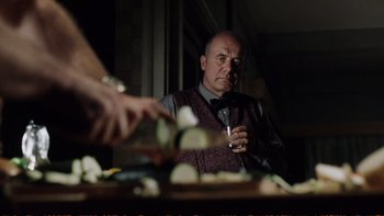Movie still from “Munich” (2005), directed by Steven Spielberg – An older man sitting at a table with a glass of wine; Medium shot, Over the shoulder angle