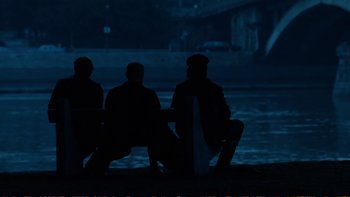 Movie still from “Munich” (2005), directed by Steven Spielberg – Three people sitting on a bench at night; Wide shot, Over the shoulder angle