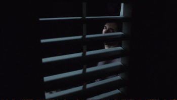 Movie still from “Munich” (2005), directed by Steven Spielberg – A man looking out of a window through blinds at night; Wide shot, Low angle