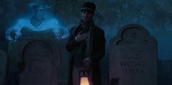 Movie still from “Muppets Haunted Mansion” (2021), directed by Kirk R. Thatcher – A man holding a lantern standing in front of two graves; Medium shot, Low angle