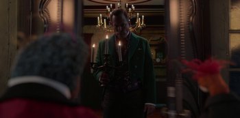 Movie still from “Muppets Haunted Mansion” (2021), directed by Kirk R. Thatcher – A man in a green jacket holding some candles; Medium shot, Over the shoulder angle