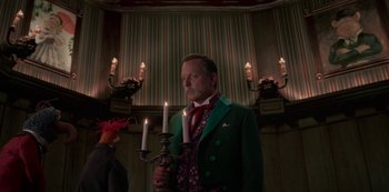 Movie still from “Muppets Haunted Mansion” (2021), directed by Kirk R. Thatcher – A man in a green jacket holding a candle holder; Medium shot, Low angle