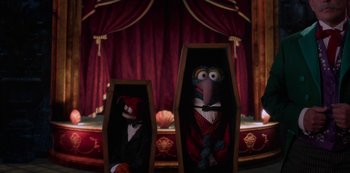 Movie still from “Muppets Haunted Mansion” (2021), directed by Kirk R. Thatcher – A couple of puppets are sitting in a casket; Wide shot, High angle