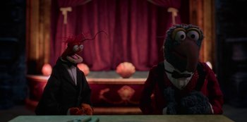 Movie still from “Muppets Haunted Mansion” (2021), directed by Kirk R. Thatcher – A couple of people sitting next to each other on top of a table; Medium shot, Over the shoulder angle