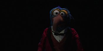Movie still from “Muppets Haunted Mansion” (2021), directed by Kirk R. Thatcher – A person wearing a bird mask and a red jacket; Medium shot, Low angle