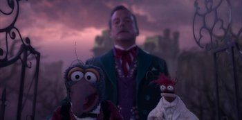 Movie still from “Muppets Haunted Mansion” (2021), directed by Kirk R. Thatcher – A man standing next to two puppets in front of a purple sky; Medium shot, Low angle