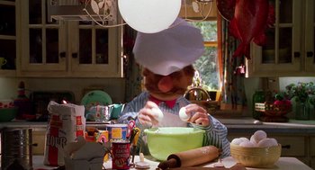 Movie still from “Muppets from Space” (1999), directed by Tim Hill – A person wearing a chef's hat while making food in a kitchen; Medium shot, Low angle
