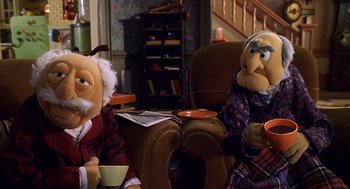 Movie still from “Muppets from Space” (1999), directed by Tim Hill – A couple of people that are sitting in a room; Medium shot, High angle