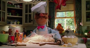 Movie still from “Muppets from Space” (1999), directed by Tim Hill – A person wearing a chef's hat sitting in front of a cake; Medium shot, Low angle