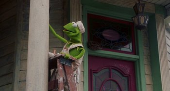 Movie still from “Muppets from Space” (1999), directed by Tim Hill – A kermit the frog puppet is painting a house; Medium shot, Low angle