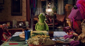 Movie still from “Muppets from Space” (1999), directed by Tim Hill – Kermit the frog sitting on a chair in front of a bowl of salad; Medium shot, Over the shoulder angle