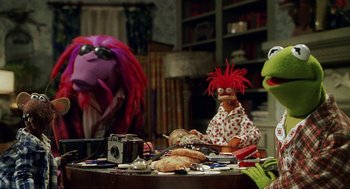 Movie still from “Muppets from Space” (1999), directed by Tim Hill – A group of stuffed animals sitting on top of a wooden table; Medium shot, Over the shoulder angle