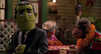 Movie still from “Muppets from Space” (1999), directed by Tim Hill – A group of people sitting at a table with a cake; Medium shot, Over the shoulder angle