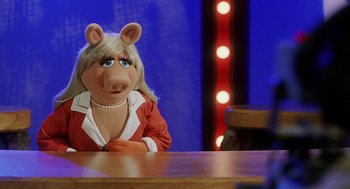 Movie still from “Muppets from Space” (1999), directed by Tim Hill – A person sitting at a table wearing a costume; Medium shot, Over the shoulder angle