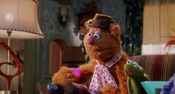 Movie still from “Muppets from Space” (1999), directed by Tim Hill – A stuffed animal wearing a hat and holding a cup; Medium shot, Over the shoulder angle