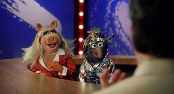 The muppets are sitting at a table talking to a man