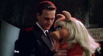 Movie still from “Muppets from Space” (1999), directed by Tim Hill – A man in a black suit and a woman in a red dress with a pig; Close Up shot, High angle