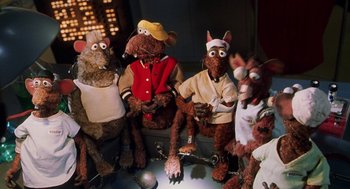 Movie still from “Muppets from Space” (1999), directed by Tim Hill – A group of stuffed animals sitting next to each other on a table; Medium shot, High angle