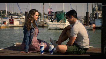 Movie still from “13 Reasons Why” (2017), created by Brian Yorkey – A man and a woman sitting on a dock by a body of water; Medium shot, Over the shoulder angle