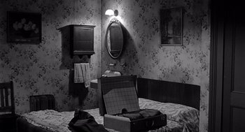 Movie still from “Murder by Contract” (1958), directed by Irving Lerner – An empty suitcase sitting on top of a bed in front of a bathroom mirror; Wide shot, High angle