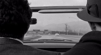 Movie still from “Murder by Contract” (1958), directed by Irving Lerner – A man driving a car on a road; Close Up shot, Over the shoulder angle