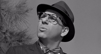 Movie still from “Murder by Contract” (1958), directed by Irving Lerner – A man in a suit and hat wearing glasses and a bow tie; Close Up shot, Low angle