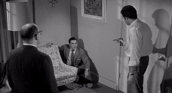 Movie still from “Murder by Contract” (1958), directed by Irving Lerner – A man sitting on a chair in a living room next to two other men; Wide shot, High angle