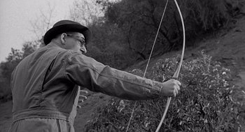 Movie still from “Murder by Contract” (1958), directed by Irving Lerner – An older man is holding a bow and arrow; Medium shot, Over the shoulder angle