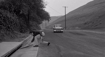 Movie still from “Murder by Contract” (1958), directed by Irving Lerner – A man on a skateboard on the side of the road; Wide shot, High angle