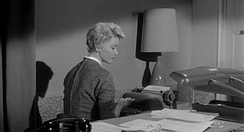 Movie still from “Murder by Contract” (1958), directed by Irving Lerner – A woman sitting at a desk typing on a typewriter; Medium shot, High angle