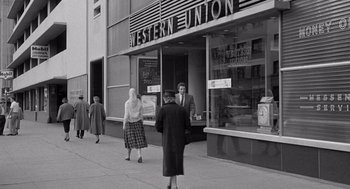 Movie still from “Murder by Contract” (1958), directed by Irving Lerner – A black - and - white photo of people walking on the sidewalk; Wide shot, Low angle