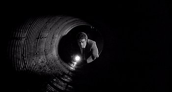 Movie still from “Murder by Contract” (1958), directed by Irving Lerner – A man is looking into a pipe with a flashlight in the dark; Wide shot, Low angle