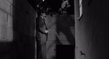 Movie still from “Murder by Contract” (1958), directed by Irving Lerner – A black and white photo of a man in a suit looking at his cell phone; Wide shot, Low angle